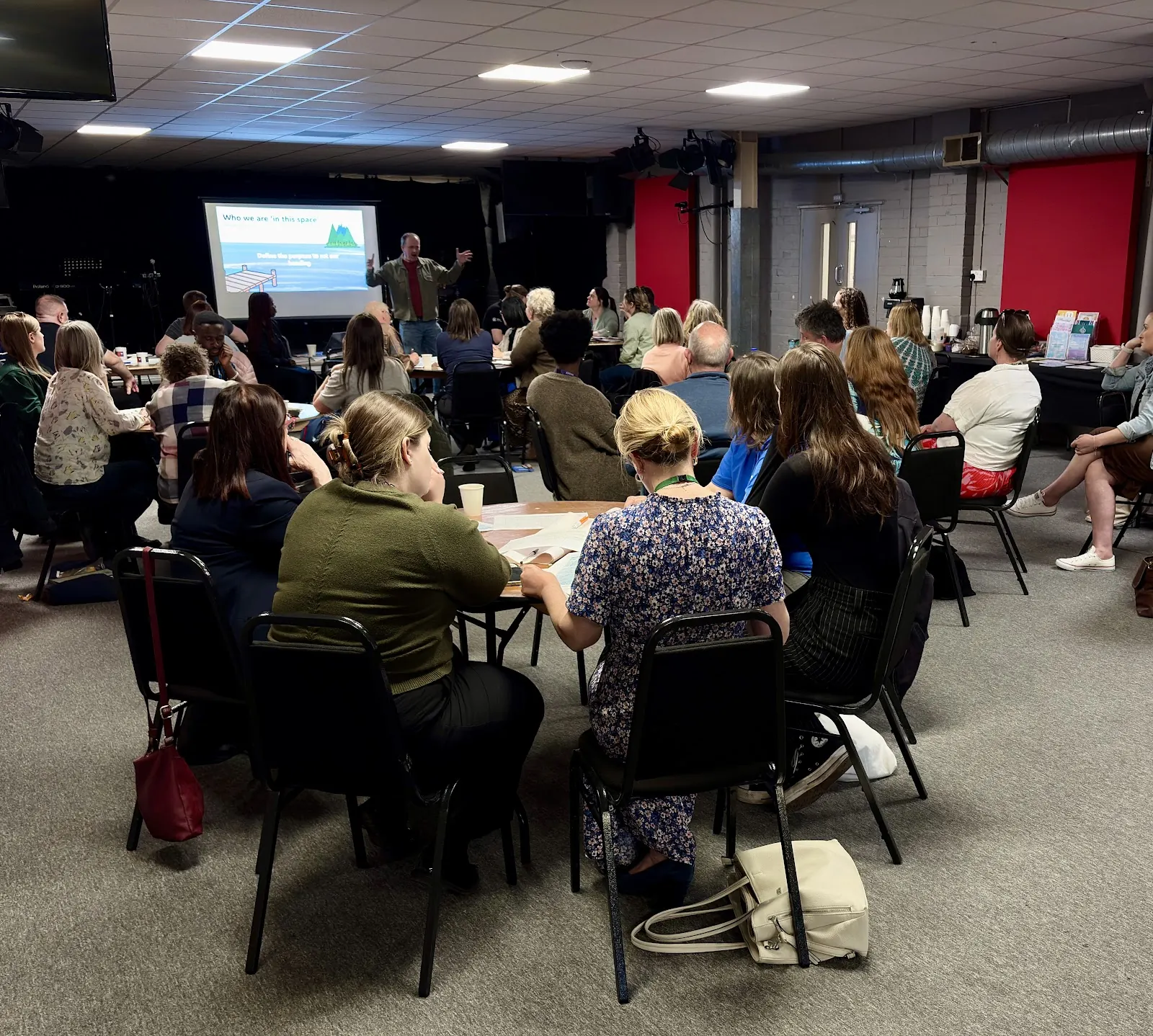 A partnership gathering: people at round tables watching a presentation