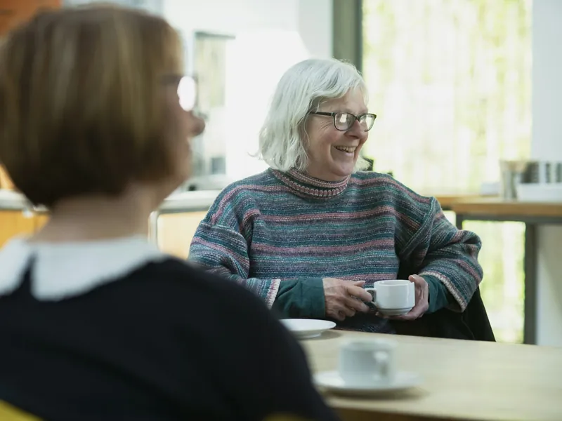 Two people talking across a table over cups of tea